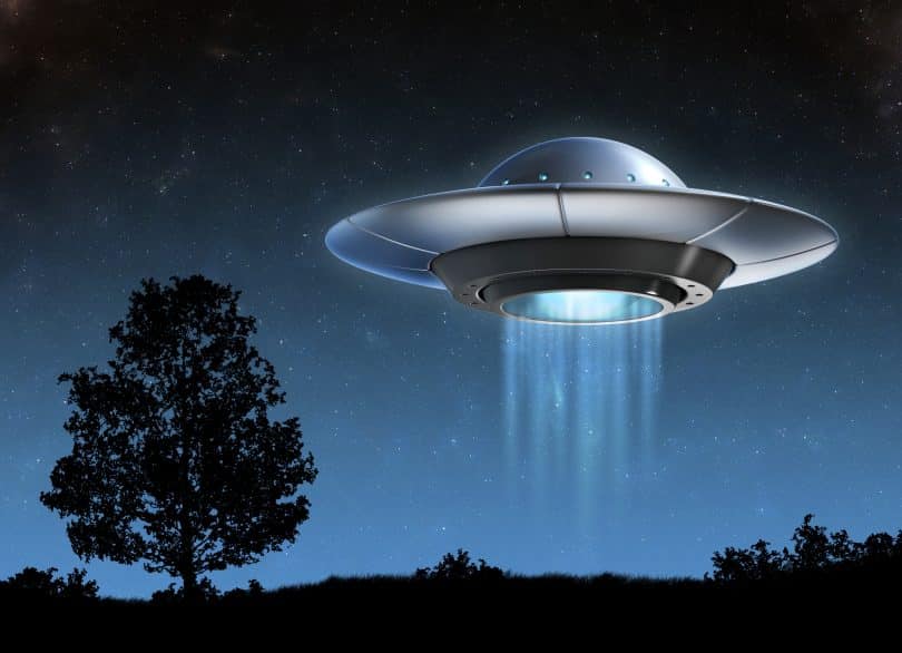 Imagem de uma nave alienígena a noite ao lado de uma árvore.
