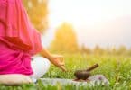 Imagem de um lindo gramado. Nele encontra-se uma mulher sentada em posição de meditação.