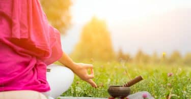 Imagem de um lindo gramado. Nele encontra-se uma mulher sentada em posição de meditação.