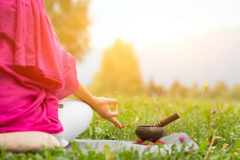 Imagem de um lindo gramado. Nele encontra-se uma mulher sentada em posição de meditação.