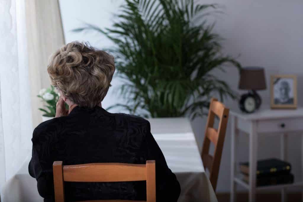 Senhora sentada na mesa de jantar de costas olhando para o lado pensativa