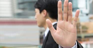 Homem na rua de roupas sociais estendendo a mão aberta como sinal de recusa.