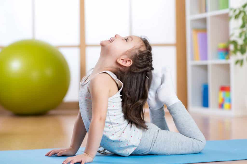 Criança fazendo yoga na sala de casa.