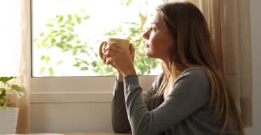 Mulher olhando para fora da janela segurando caneca de café