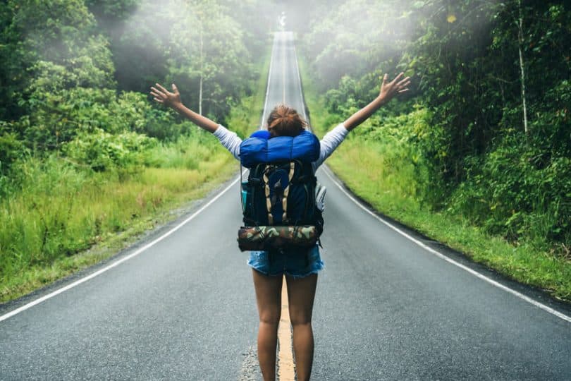 Mulher de costas com braços abertos e estrada em frente