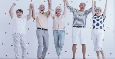 Grupo de cinco idosos sorrindo com as mãos para cima.