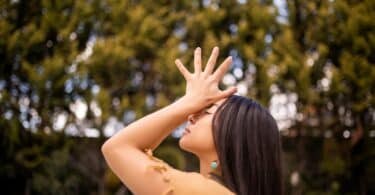 Imagem de uma mulher com as mãos para os altos. Ao fundo, várias árvores completam a foto que traz o conceito de busca pela paz interior.