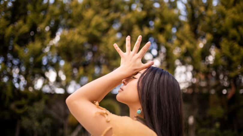 Imagem de uma mulher com as mãos para os altos. Ao fundo, várias árvores completam a foto que traz o conceito de busca pela paz interior.