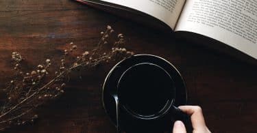 Mulher segurando xícara de chá ao lado de um livro aberto