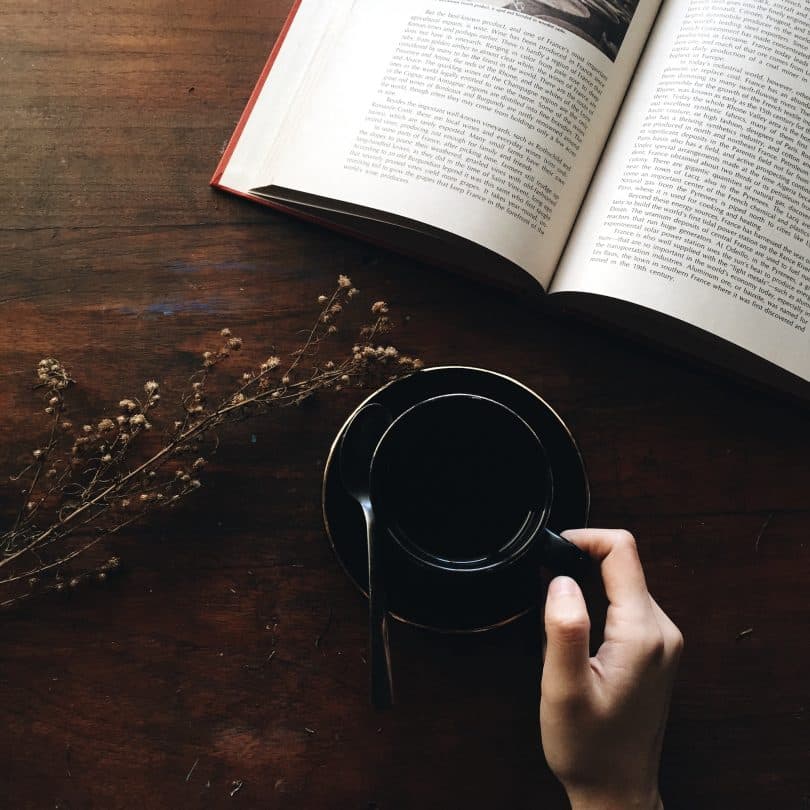 Mulher segurando xícara de chá ao lado de um livro aberto