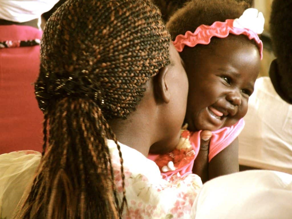 Linda bebê africana no colo de sua mãe. Ela está sorrindo.