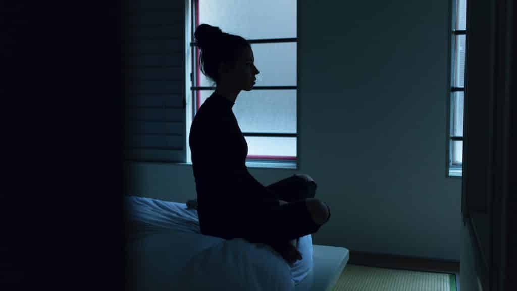 Mulher sentada na cama em seu quarto escuro com luz saindo da janela