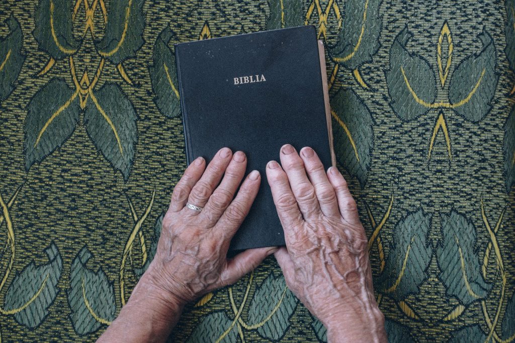 Imagem da bíblia fechada e sobre ela as mãos de uma senhora idosa. Ela está exercendo a sua espiritualidade.