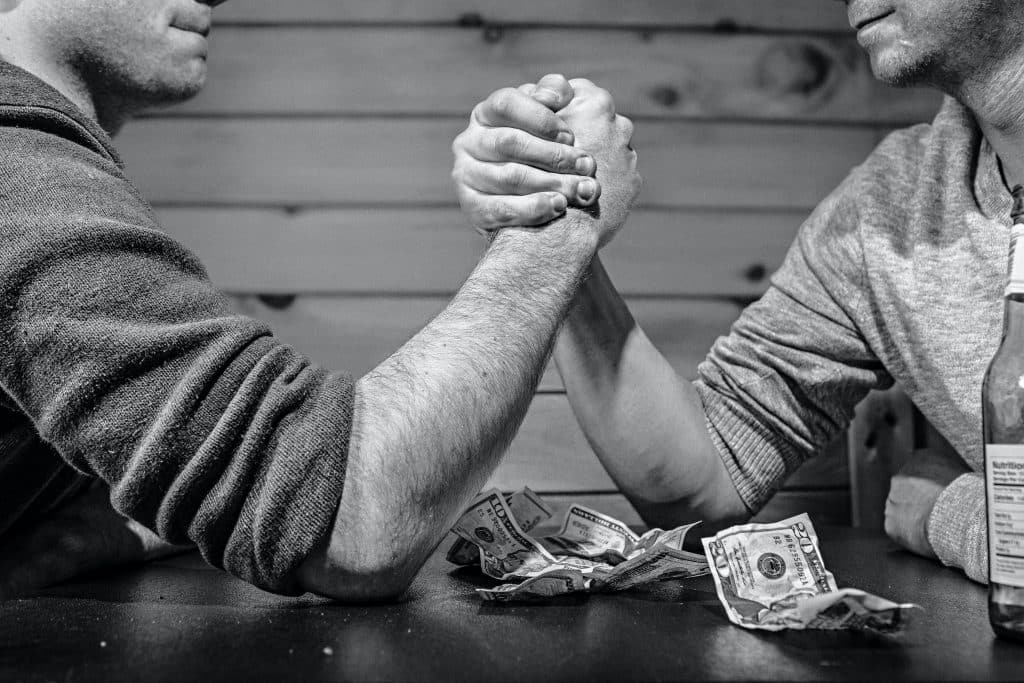 Dois homens sentados em uma mesa apostando dinheiro em uma queda de braço.