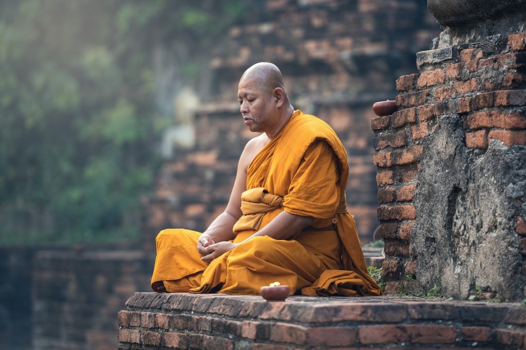Imagem de um monge sentado no chão em posição de meditação.