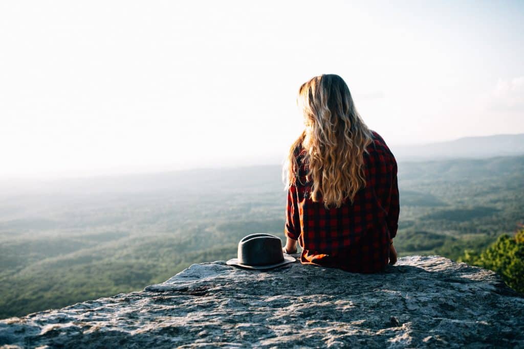 Mulher sentada em uma montanha olhando para o horizonte