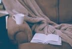 Sofá com livro aberto, caneca e cobertor