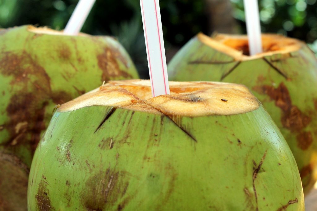 Imagem de três cocos verdes com canudos prontos para serem consumidos.