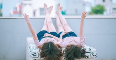 Imagem de duas garotas deitadas sobre uma cama. Elas estão com as pernas para cima contemplando o lindo dia.