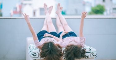 Imagem de duas garotas deitadas sobre uma cama. Elas estão com as pernas para cima contemplando o lindo dia.