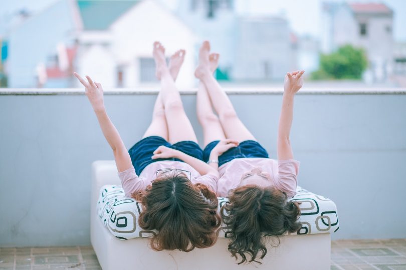 Imagem de duas garotas deitadas sobre uma cama. Elas estão com as pernas para cima contemplando o lindo dia.