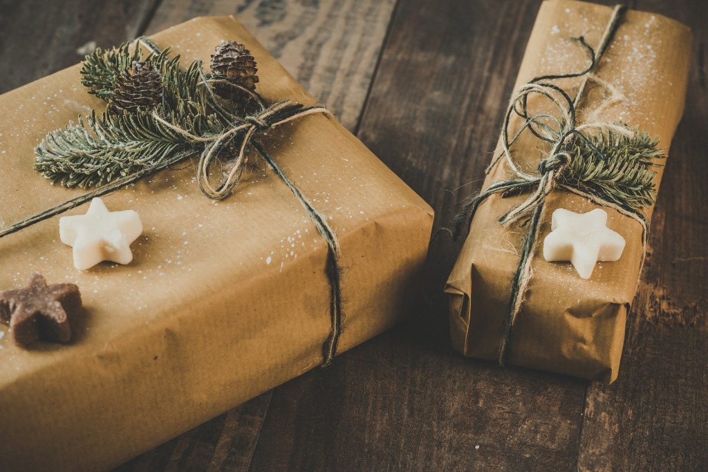 Imagem de duas caixas de presentes embrulhadas em papel pardo e decoadas com enfeites natalinos como estrelas, pinha e folhas da árvore de Natal.