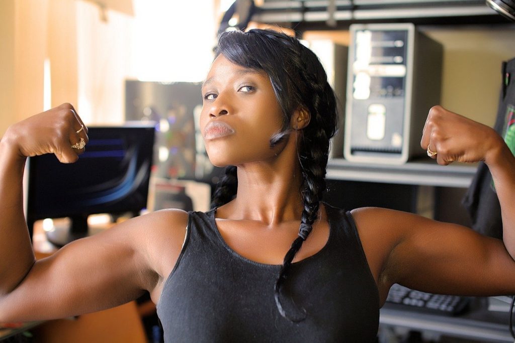 Imagem de uma linda mulher negra mostrando os seus músculos, represetando a força e a igualdade de gênero.
