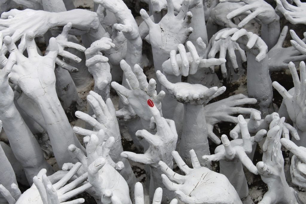 Imagem em preto e branco de vãrias mãos femininas e no centro uma mão com um dedo em destaque com a sua unha pintada na cor vermelha.
