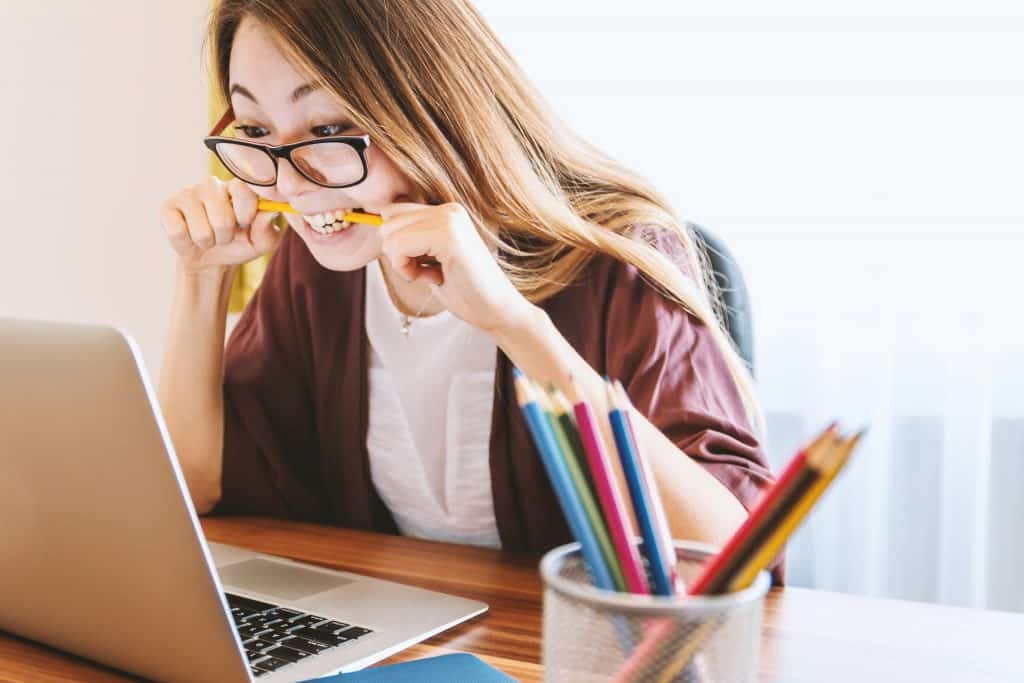 Mulher mordendo um lápis em frente a um computador, em sinal de estresse.