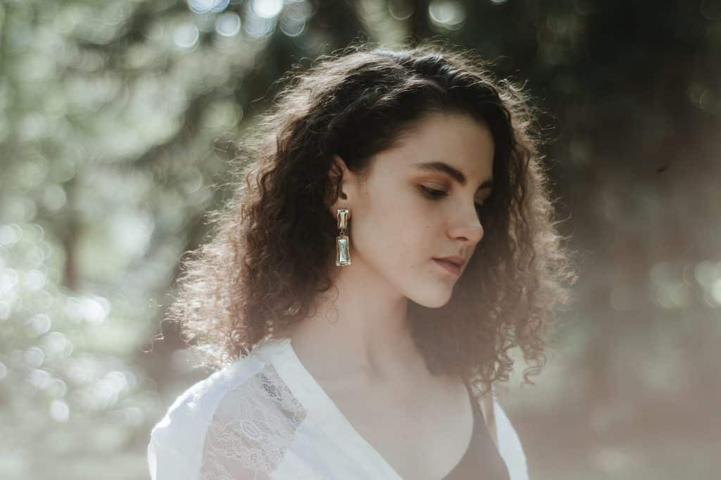 Retrato de uma mulher de cabelos cacheados, em um parque, olhando para baixo.