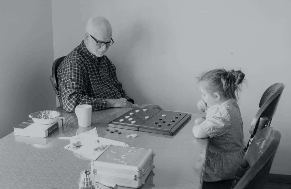 Menina sentada à mesa jogando damas com seu avô.