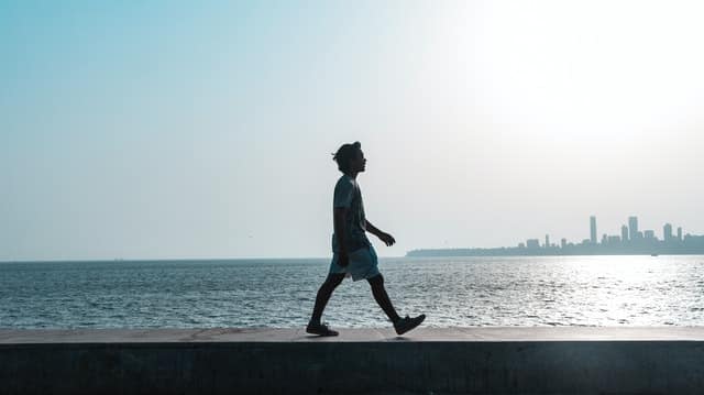 Homem caminhando em parapeito com mar ao fundo