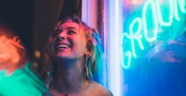 Mulher sorrindo ao lado de um letreiro de neon