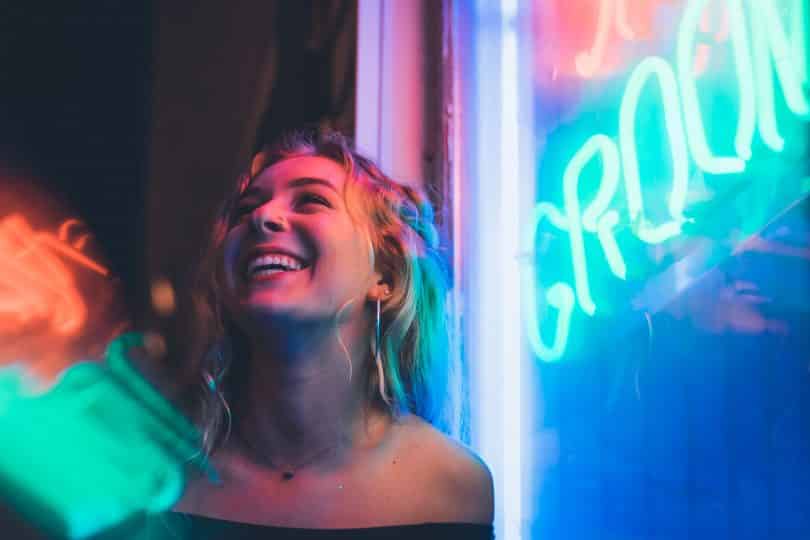 Mulher sorrindo ao lado de um letreiro de neon