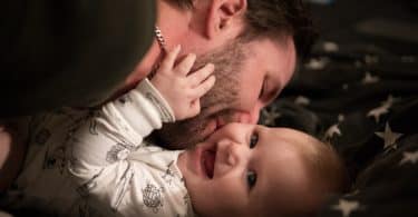 Pai beijando bochecha do bebê sorrindo deitado na cama