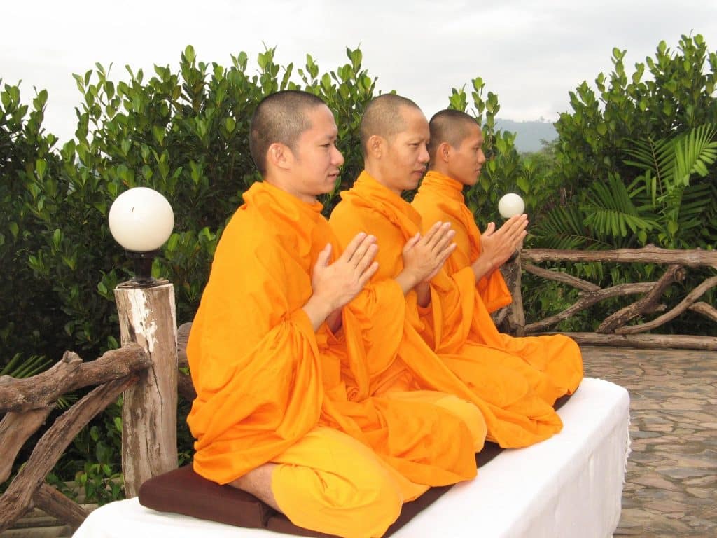 Imagem de três monges praticando a meditação.
