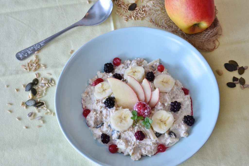 Imagem de um prato fundo de porcelana branca com cereais e frutas como banana, maça e framboesa.