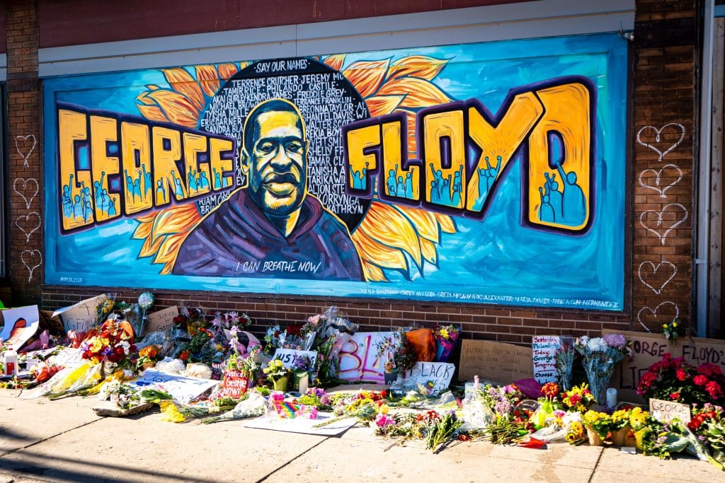 Homenagem para George Floyd com um grafite em um muro e cartazes, flores no chão