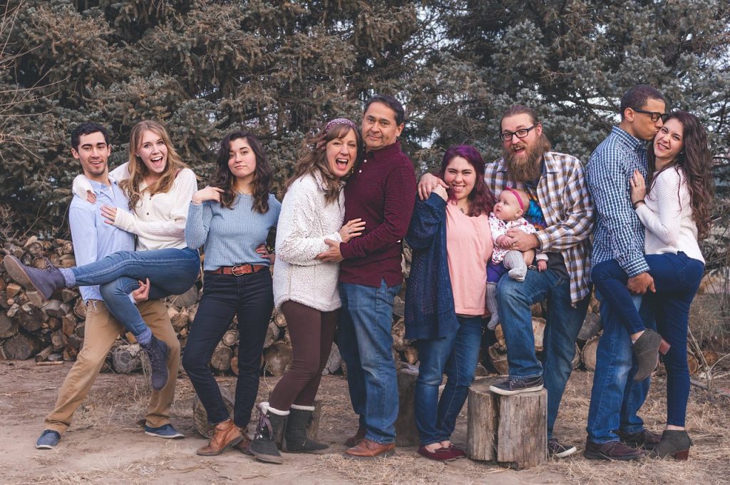 Foto de uma família reunida em um parque com árvores, com todos os membros lado a lado, sorrindo e se abraçando.