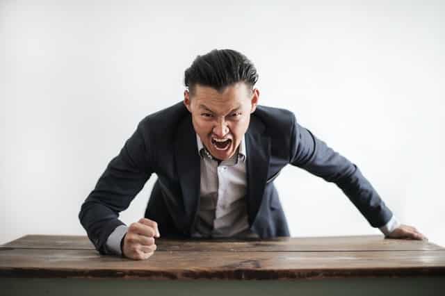 Homem com raiva batendo na mesa de madeira