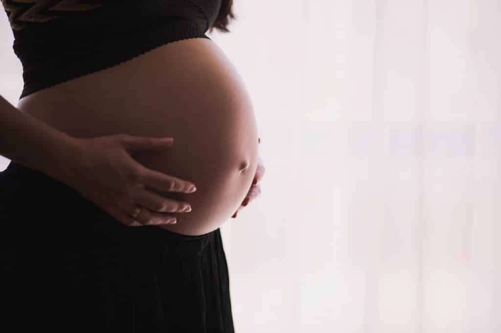 Mulher grávida com as mãos sobre a barriga.