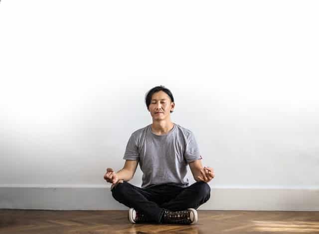 Homem sentado em posição de lótus de olhos fechados meditando