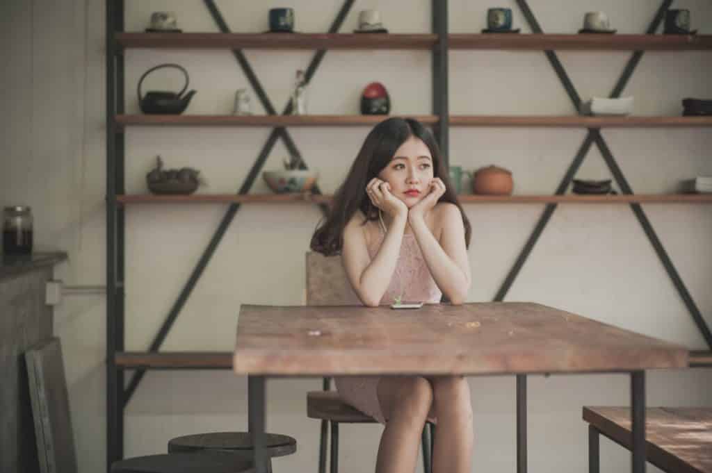 Mulher jovem de vestido, apoiando a cabeça nas mãos com expressão frustrada.