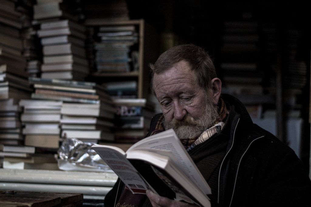 Imagem de um homem na terceira idade lendo o livro sobre Kepler. Ee está em uma biblioteca.
