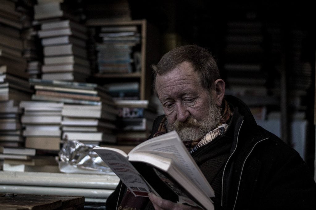 Imagem de um homem na terceira idade lendo o livro sobre Kepler. Ee está em uma biblioteca.
