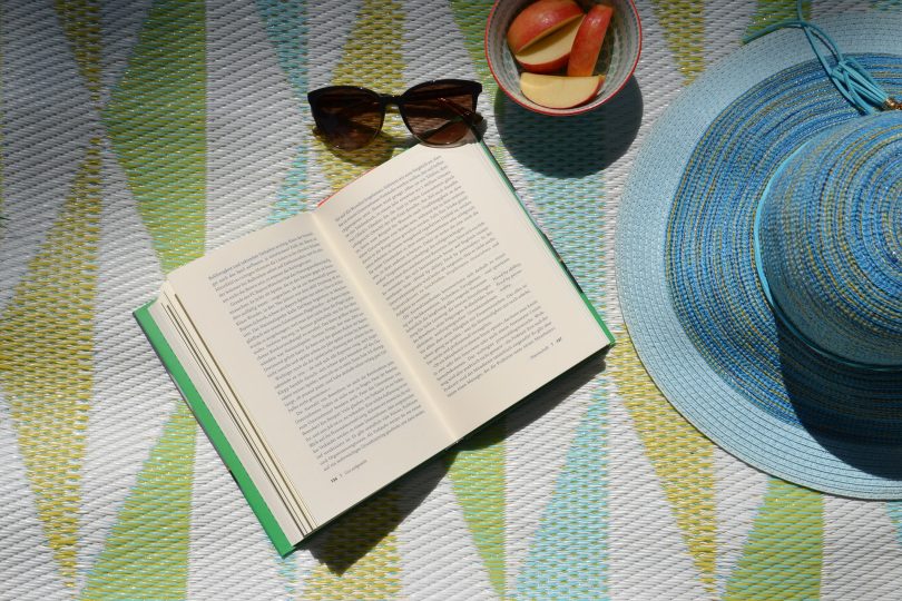 Imagem de um livro, óculos e chapéu de sol e um pote com maça cortada. Elementos que ajudam acalmar a mente e relaxar.