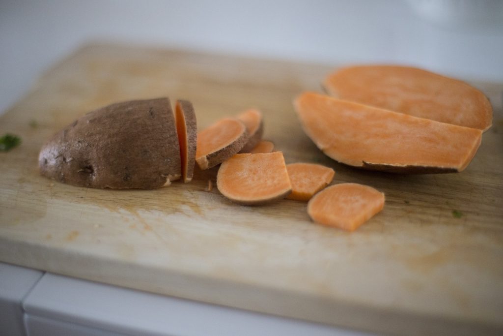 Imagem de uma batata doce sobre uma tábua de madeira. Ela está cortada em pedaços grandes e pequenos. Ela ajuda a aumentar a libido.
