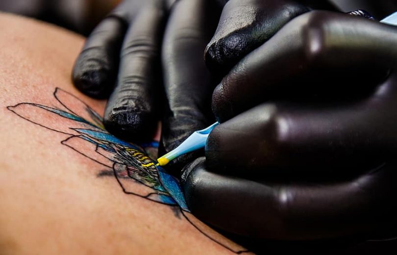 Tatuador preenchendo a figura de uma flor de lótus na pele de uma pessoa.