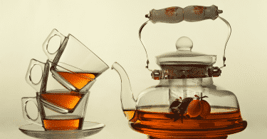 Imagem de uma chaleira de vidro moderna e ao lado três xícaras de vidro uma sobre a outra. A chaleira está com Chá caseiro para dor de estômago.