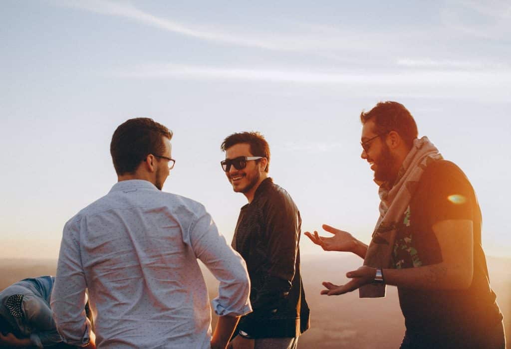 Três homens caminhando e conversando ao pôr do sol.